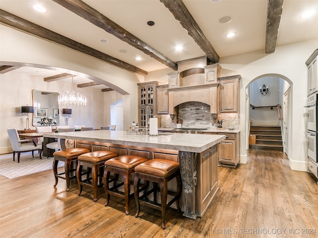 kitchen with a breakfast bar area, arched walkways, a kitchen island with sink, and backsplash