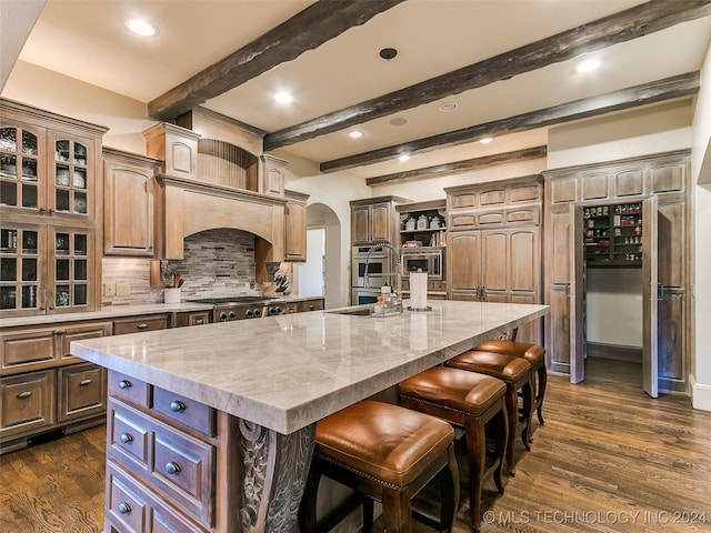 kitchen with a kitchen island with sink, dark wood-style floors, arched walkways, and appliances with stainless steel finishes