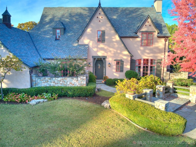 tudor-style house featuring a front lawn, stucco siding, and a chimney