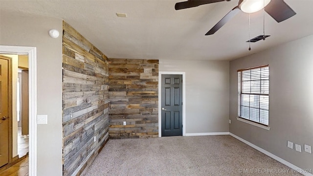 carpeted empty room with ceiling fan and wood walls