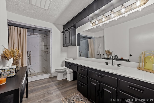 bathroom with a textured ceiling, a tile shower, hardwood / wood-style floors, vanity, and toilet