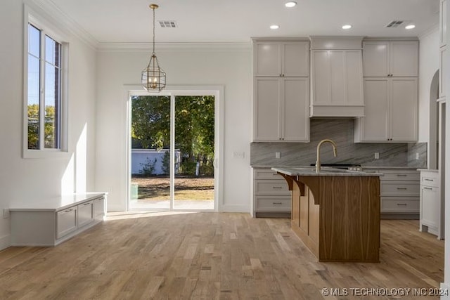 kitchen featuring ornamental molding, a kitchen island, backsplash, hanging light fixtures, and light hardwood / wood-style floors