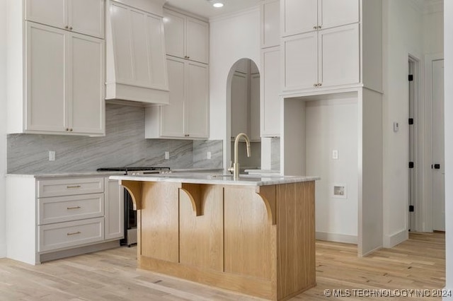 kitchen with white cabinets, light hardwood / wood-style flooring, premium range hood, and an island with sink