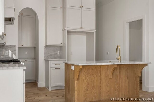 kitchen with sink, an island with sink, light hardwood / wood-style flooring, white cabinets, and decorative backsplash