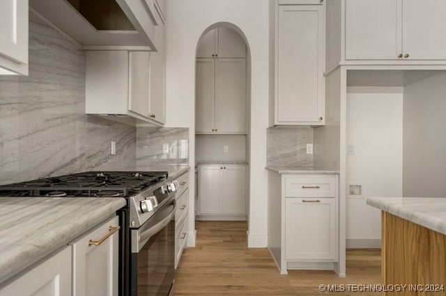 kitchen with light stone counters, white cabinets, tasteful backsplash, gas stove, and light hardwood / wood-style flooring