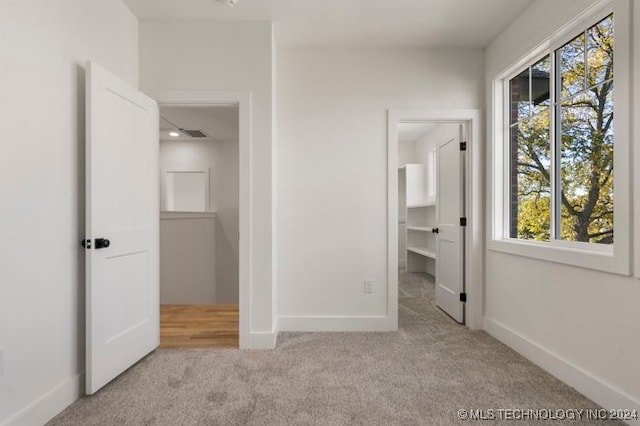 unfurnished bedroom featuring a walk in closet and light colored carpet