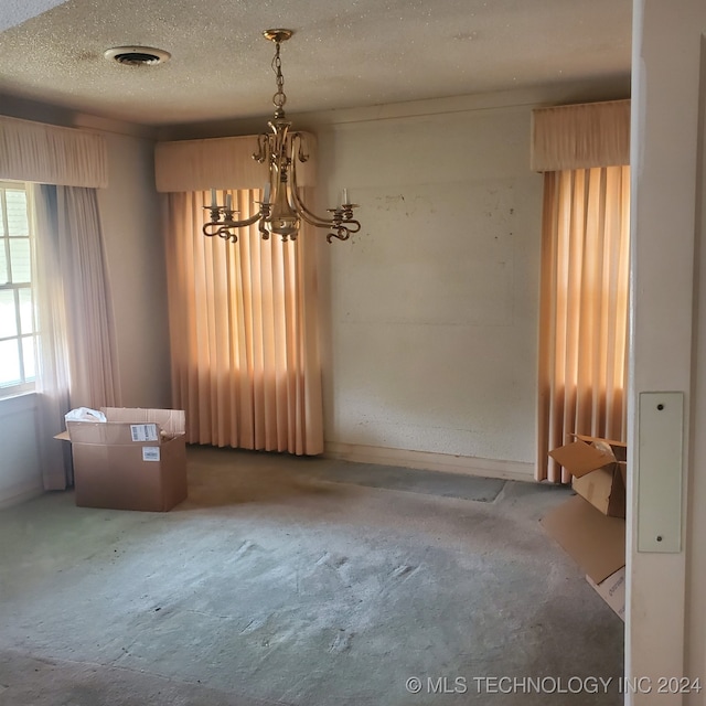 empty room with concrete flooring, a textured ceiling, and an inviting chandelier