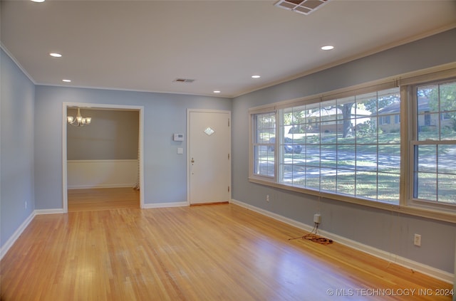 foyer featuring light wood-type flooring, crown molding, and a notable chandelier