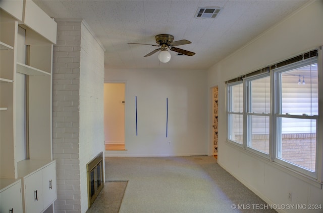 unfurnished living room featuring a large fireplace, light colored carpet, ceiling fan, and crown molding