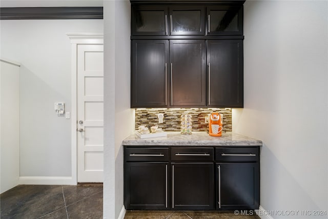 bar featuring dark tile patterned floors, backsplash, light stone counters, and ornamental molding