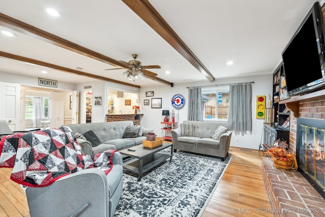 living room with a brick fireplace, hardwood / wood-style floors, ceiling fan, and beam ceiling