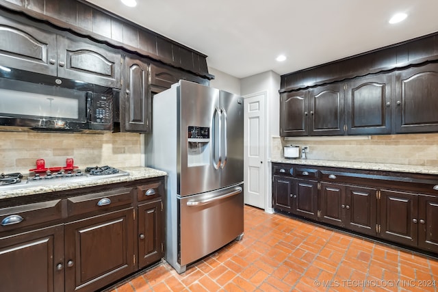 kitchen featuring stainless steel appliances, light stone countertops, backsplash, and dark brown cabinetry