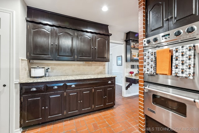 kitchen with tasteful backsplash, light stone countertops, dark brown cabinets, and double oven