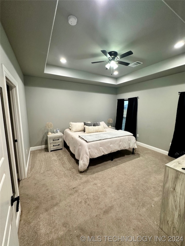 carpeted bedroom featuring ceiling fan and a raised ceiling