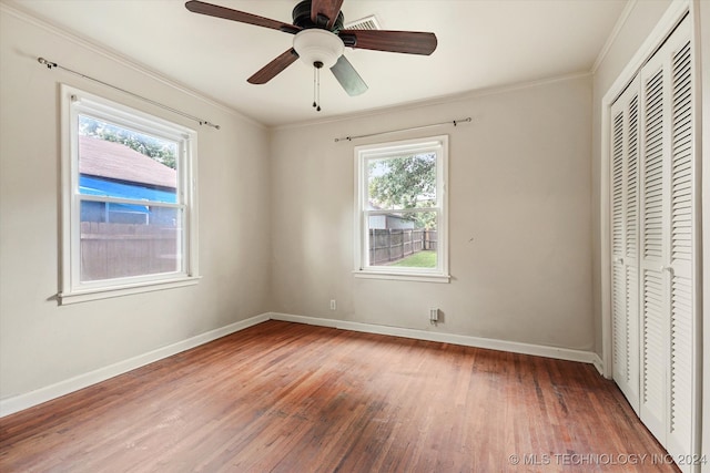 unfurnished bedroom with a closet, multiple windows, hardwood / wood-style floors, and ceiling fan