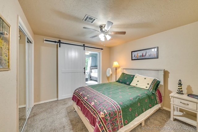 bedroom featuring carpet floors, a textured ceiling, a barn door, ceiling fan, and a closet