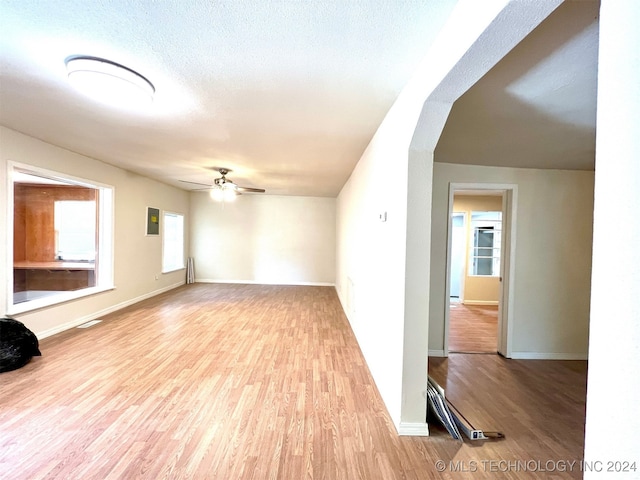 unfurnished living room with a textured ceiling, ceiling fan, and light hardwood / wood-style flooring