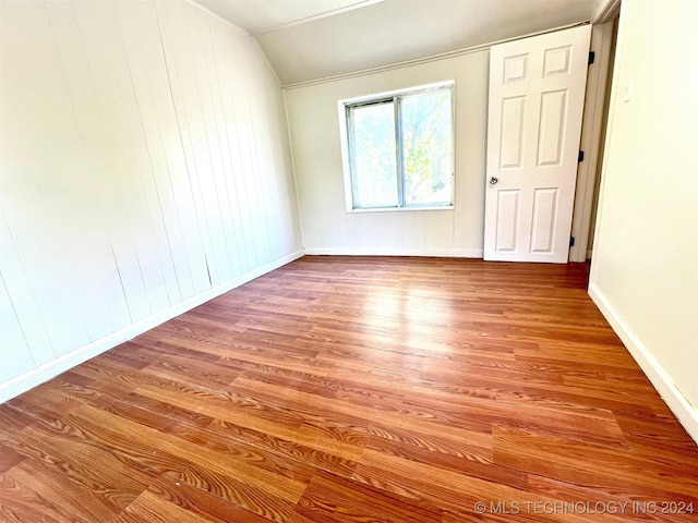 empty room featuring wood walls, lofted ceiling, and wood-type flooring