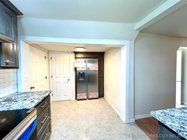 kitchen featuring light stone counters, decorative backsplash, range, stainless steel fridge with ice dispenser, and dark brown cabinets