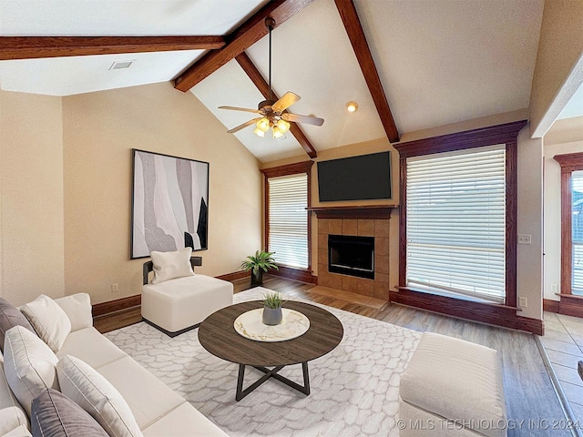 living room with lofted ceiling with beams, plenty of natural light, a tile fireplace, and light hardwood / wood-style flooring