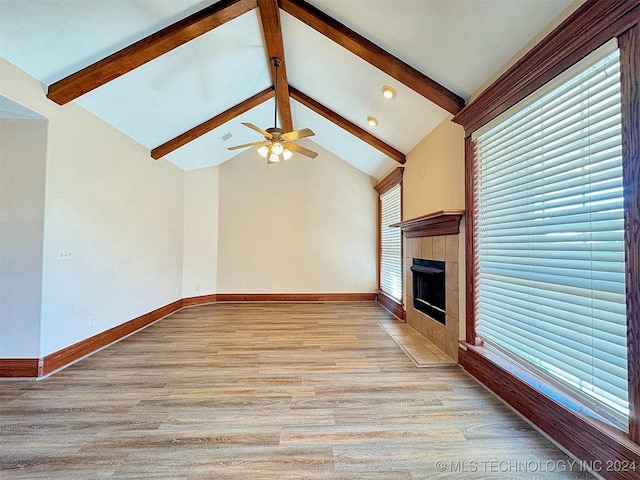 unfurnished living room with light wood-type flooring, plenty of natural light, lofted ceiling with beams, and a tile fireplace