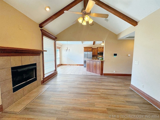 unfurnished living room featuring ceiling fan with notable chandelier, a tile fireplace, light wood-type flooring, and lofted ceiling with beams