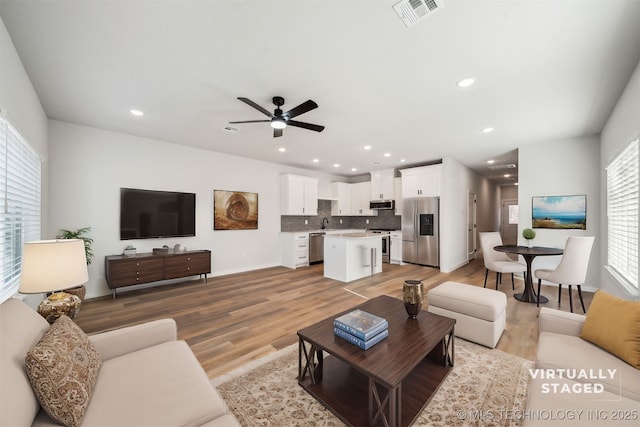 living room featuring ceiling fan, sink, and light hardwood / wood-style flooring