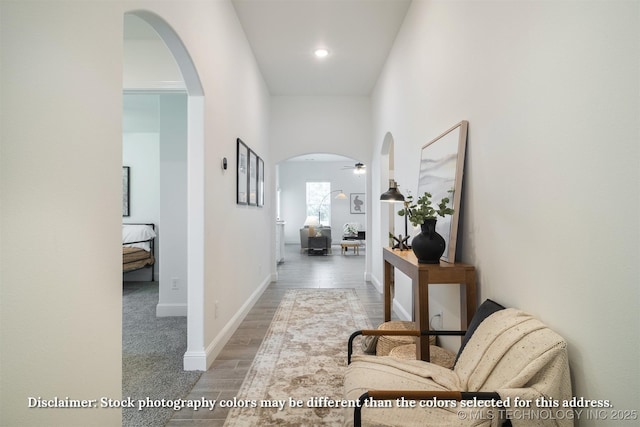 corridor with arched walkways, baseboards, and wood finished floors