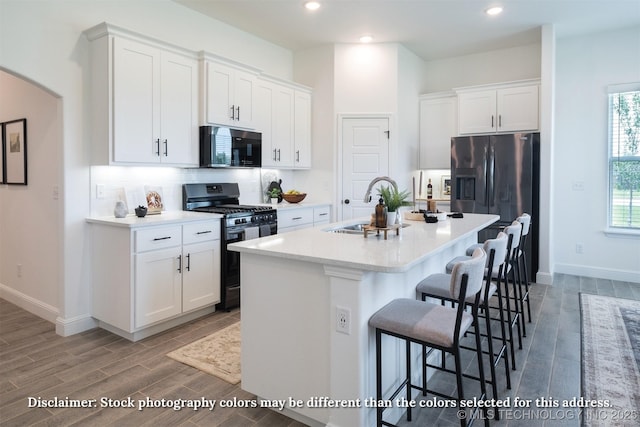 kitchen with black microwave, gas range oven, an island with sink, and white cabinets