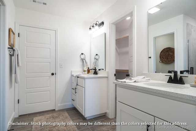 full bathroom featuring visible vents, two vanities, a spacious closet, wood tiled floor, and a sink