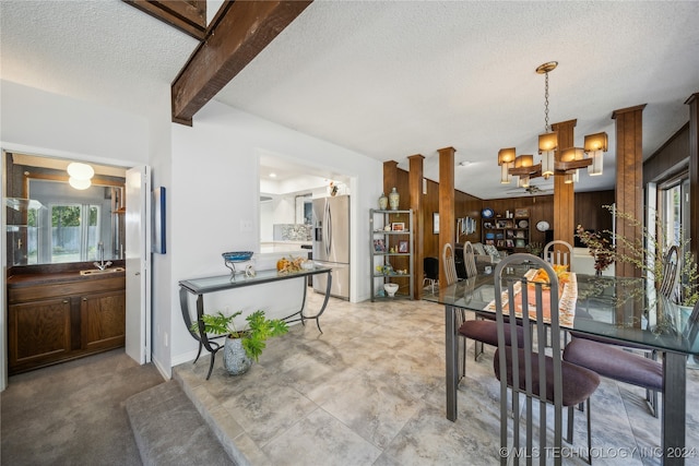 dining space with an inviting chandelier, beamed ceiling, decorative columns, wood walls, and a textured ceiling