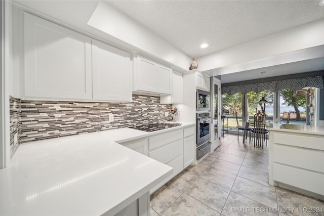 kitchen featuring decorative backsplash, black electric stovetop, white cabinetry, and hanging light fixtures