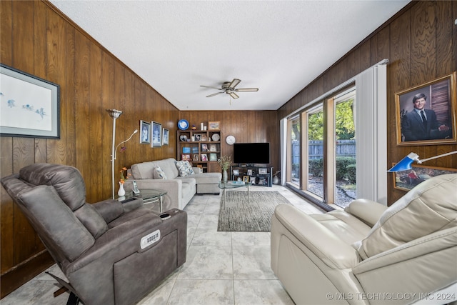 tiled living room with ceiling fan, wood walls, and a textured ceiling