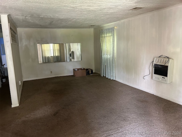 spare room featuring a textured ceiling, dark colored carpet, a healthy amount of sunlight, and heating unit