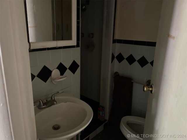 bathroom with tile walls, sink, toilet, and a shower