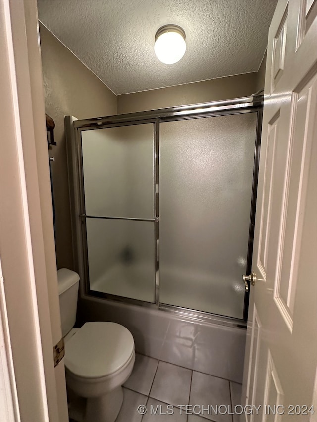 bathroom with toilet, bath / shower combo with glass door, a textured ceiling, and tile patterned floors