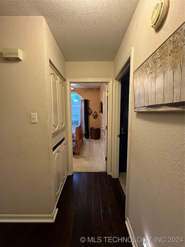 corridor with dark hardwood / wood-style flooring and a textured ceiling