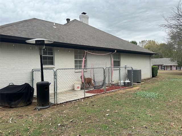 rear view of house with central AC unit and a yard