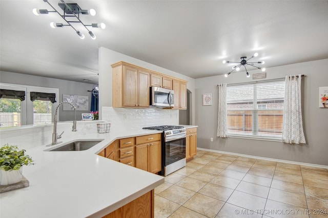 kitchen with kitchen peninsula, tasteful backsplash, stainless steel appliances, sink, and a notable chandelier