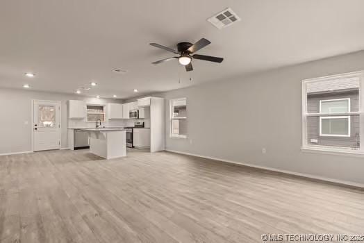 unfurnished living room with light wood-type flooring, baseboards, visible vents, and a ceiling fan