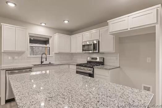 kitchen with light stone counters, stainless steel appliances, a sink, white cabinetry, and a center island