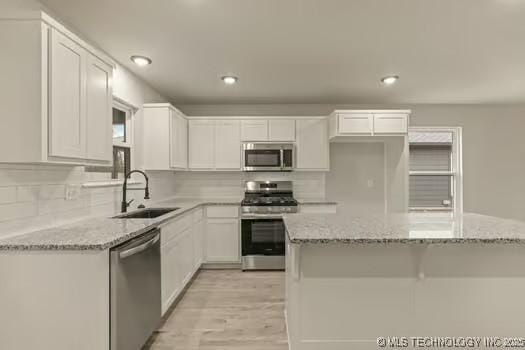 kitchen with appliances with stainless steel finishes, white cabinetry, a sink, and light stone counters