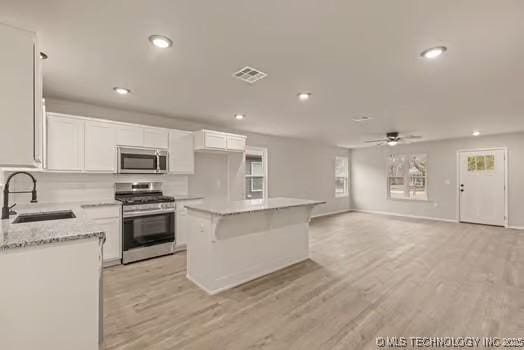 kitchen featuring stainless steel appliances, a sink, light wood-style flooring, and white cabinets