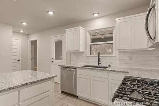 kitchen featuring backsplash, white cabinets, a sink, light stone countertops, and dishwasher