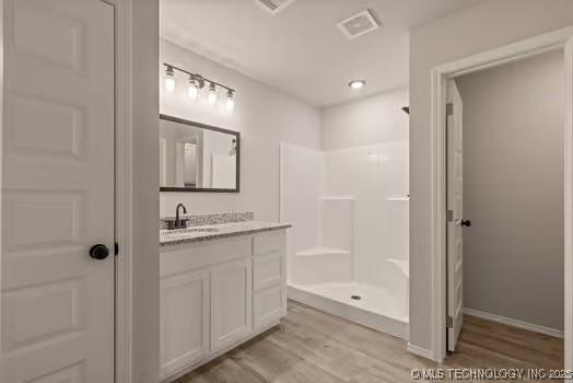 full bath featuring a shower, visible vents, vanity, wood finished floors, and baseboards