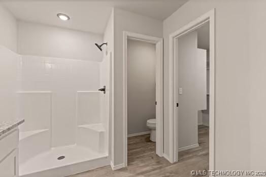 full bath featuring toilet, baseboards, walk in shower, and wood finished floors