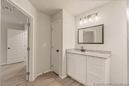 bathroom with visible vents, vanity, baseboards, and wood finished floors