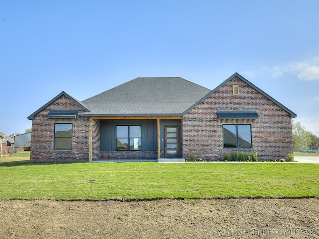 view of front of house featuring roof with shingles, a front yard, and brick siding