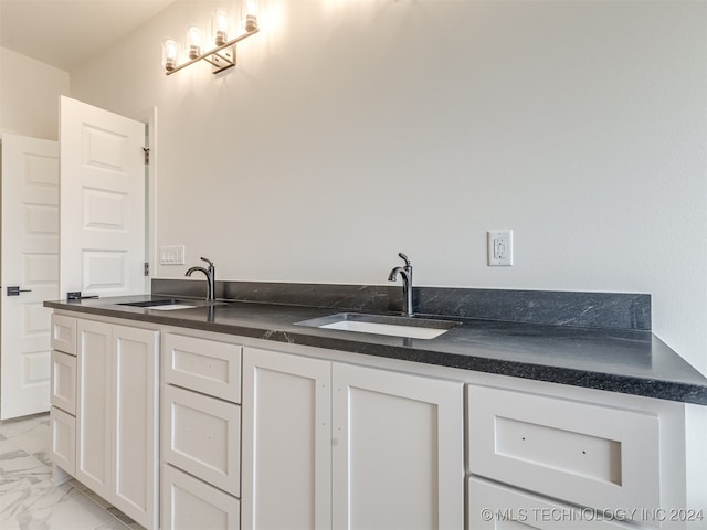 kitchen with dark countertops, marble finish floor, white cabinets, and a sink