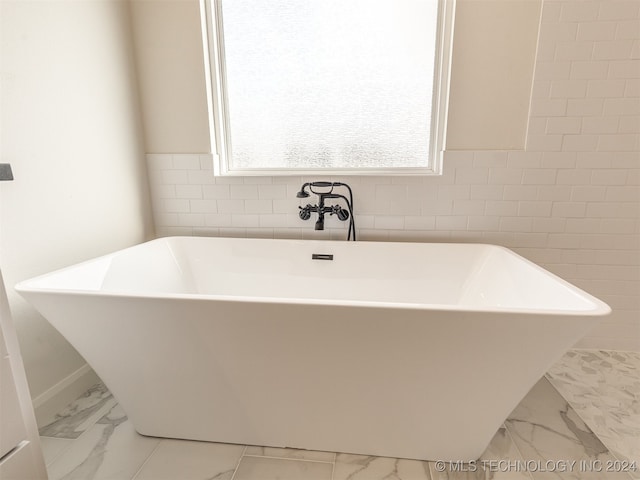 full bath with marble finish floor, tile walls, and a soaking tub